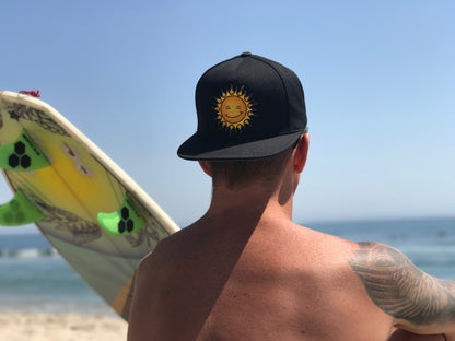Man looking away toward the ocean with a surf board wearing a new blackKine Threads OG Twill Snapback Hat backwards on his head